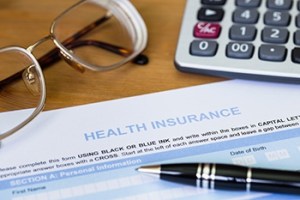 A calculator, pen, health insurance form and pair of glasses